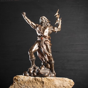 K&ouml;nnte beinhalten: Eine Bronzestatue von Zeus, dem griechischen Gott des Himmels und des Donners, der einen Blitz in seiner rechten Hand h&auml;lt. Die Statue steht auf einem Steinsockel mit der Aufschrift "ZEUS".
