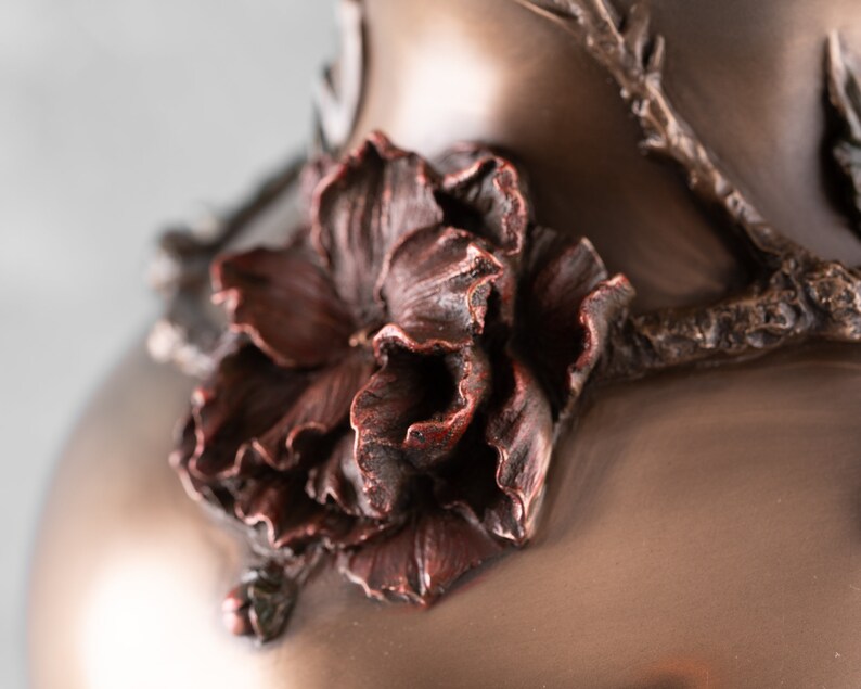 Puede incluir: Primer plano de un jarr&oacute;n de bronce con un dise&ntilde;o floral detallado. El jarr&oacute;n presenta una sola flor con un acabado texturizado marr&oacute;n rojizo.