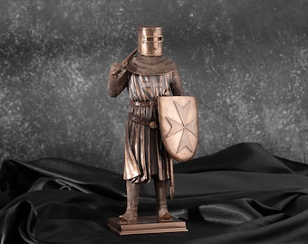 May include: A bronze statue of a knight wearing chainmail armor and a helmet with a cross on the chest. The knight is holding a sword and a shield with a cross on it.