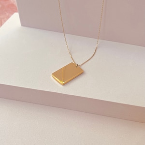 Könnte beinhalten: Eine goldene Kettenkette mit einem rechteckigen Anhänger.