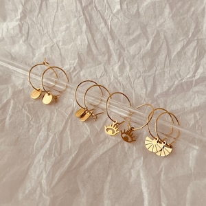 Könnte beinhalten: Set aus goldenen Creolen mit verschiedenen Anhängern, darunter Kreise, Augen und eine Fächerform.