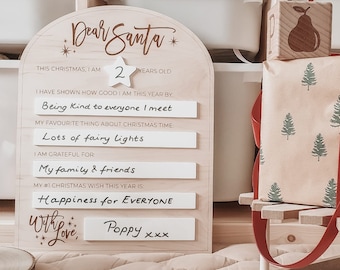 May include: A wooden Christmas letter to Santa with a handwritten message. The letter is decorated with stars and snowflakes. The letter is next to a wooden sled with a wrapped gift box.