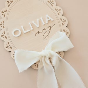 close-up of maple wood scalloped sign with 3D white acrylic baby name and soft off-white ribbon, ideal for baby announcement or shelf decor.