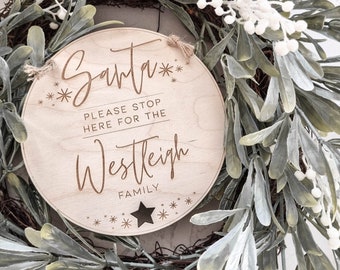 May include: A round wooden sign with the text "Santa** Please stop here for the Westleigh Family**" in a brown font. The sign is decorated with stars and is hanging on a green wreath.