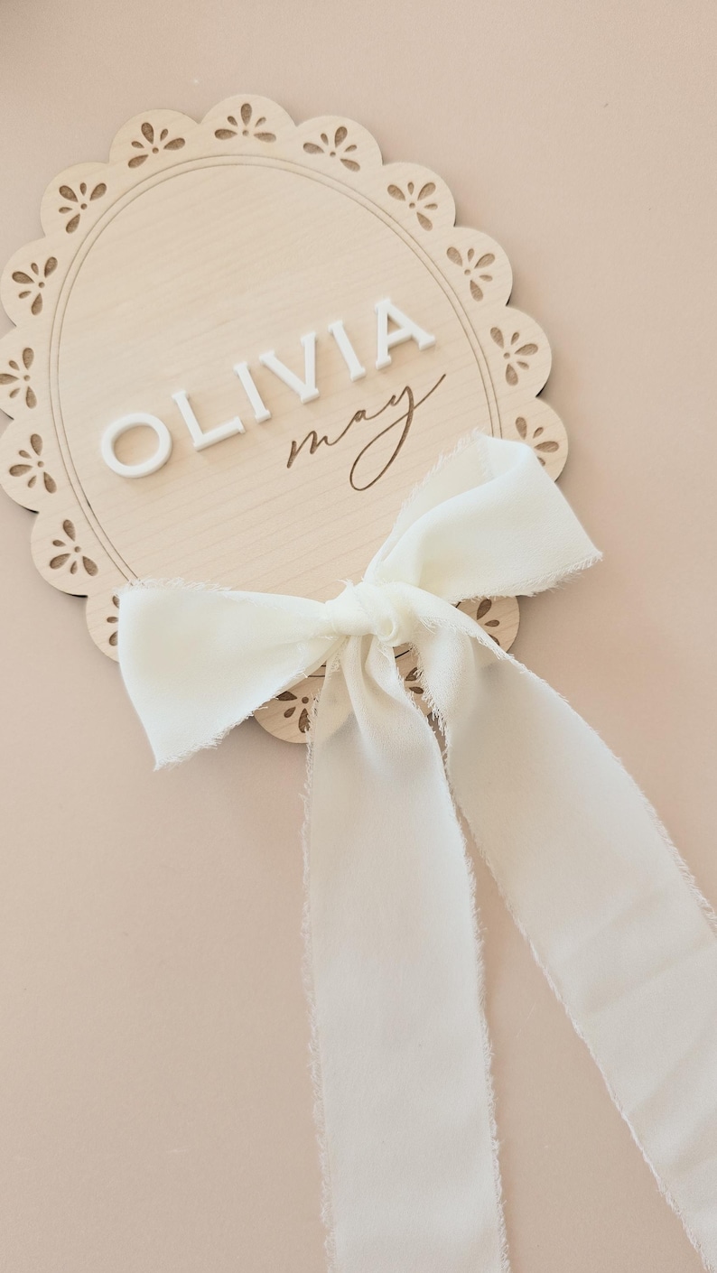 close-up of maple wood scalloped sign with 3D white acrylic baby name and soft off-white ribbon, ideal for baby announcement or shelf decor.