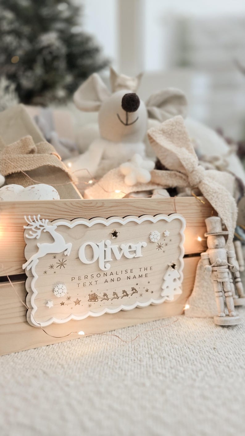 May include: A wooden sign with the name "Oliver" in white, surrounded by decorative elements like a reindeer, snowflakes, and a Christmas tree. The sign is part of a Christmas-themed display.