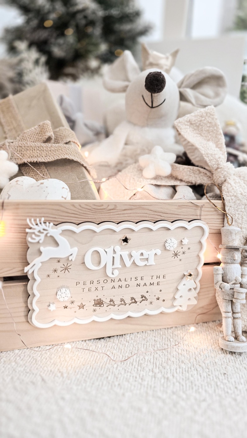 May include: A wooden crate with a personalized sign that reads "Oliver". The sign has a white border with decorative elements like a reindeer, snowflakes, and a Christmas tree. The crate is filled with gifts and a plush mouse.