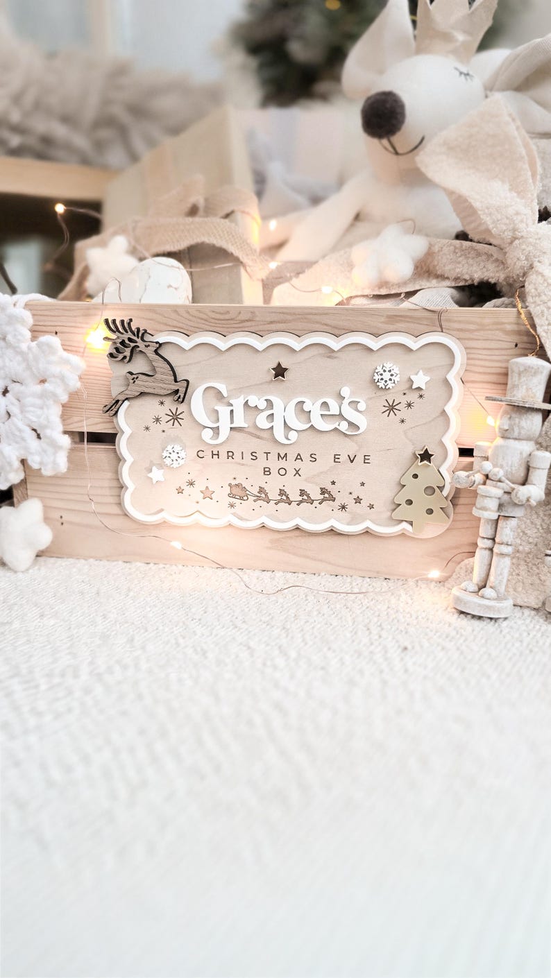 May include: A wooden Christmas Eve box with the name "Grace's" and the text "Christmas Eve Box" in white. The box is decorated with a reindeer, stars, a Christmas tree, and a sleigh with reindeer. A wooden toy soldier stands to the right.