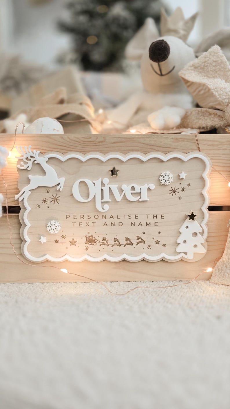 May include: Wooden sign with the name "Oliver" in white, featuring a reindeer, snowflakes, stars, and a Christmas tree. The sign includes the text "Personalise the text and name" and a sleigh with reindeer.