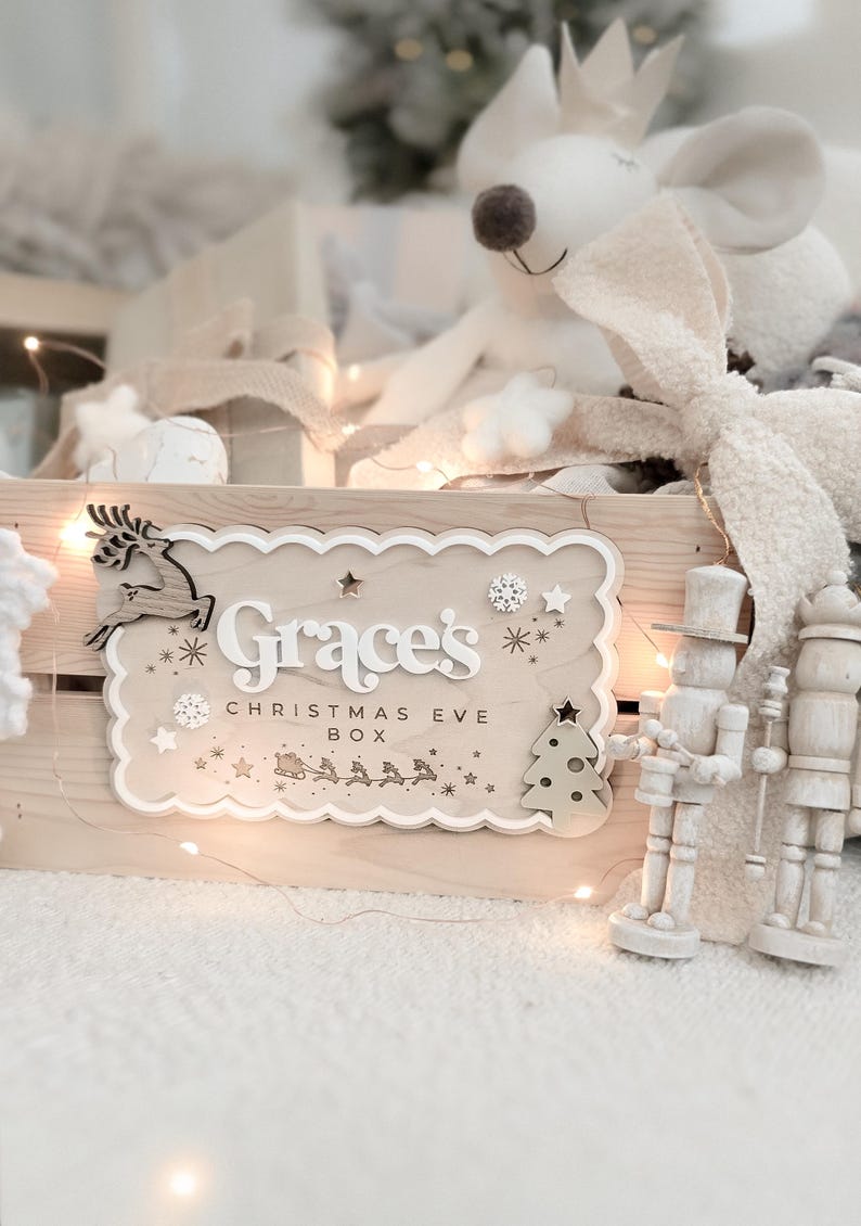 May include: A wooden Christmas Eve box with the name "Grace's" and the text "Christmas Eve Box" in white lettering. The box is decorated with a reindeer, stars, snowflakes, and a Christmas tree. A plush mouse and nutcrackers are also visible.