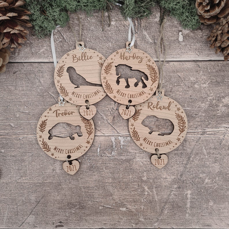 May include: Four wooden Christmas ornaments with personalized names, animal silhouettes, and the year 2021. The ornaments are Billie with a bird, Tredor with a turtle, Hardey with a horse, and Roland with a guinea pig.
