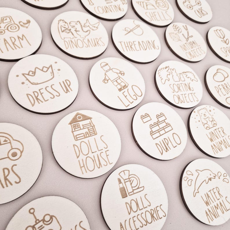 May include: A set of 16 wooden circle toy labels with various images and text, including "Farm", "Dress Up", "Dinosaurs", "Threading", "Lego", "Dolls House", "Duplo", "Water Animals", and "Dolls Accessories".