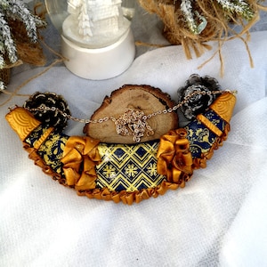 May include: A gold and blue necklace with a geometric pattern and gold trim. The necklace is made of polymer clay and has a crescent moon shape.