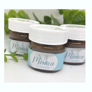 Könnte beinhalten: Drei kleine Glasgefäße mit weißen Deckeln und braunem Inhalt. Jedes Gefäß hat ein blaues und weißes Etikett mit dem Namen "Monica" und dem Datum "21.05.2023".