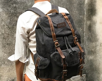 May include: A black canvas backpack with brown leather straps and buckles. The backpack has a large main compartment, two front pockets, and a drawstring closure. The backpack has a leather patch with the text "MSK" on the front.