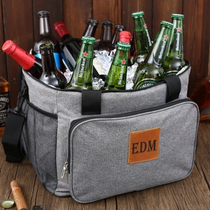 May include: A gray insulated cooler bag with a brown leather patch that says "EDM". The bag is filled with ice and bottles of beer.