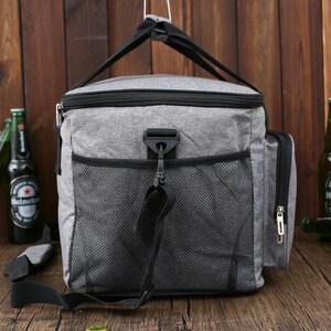 May include: A gray and black insulated cooler bag with a zippered front pocket and a mesh side pocket. The bag has a black adjustable shoulder strap and a top handle.