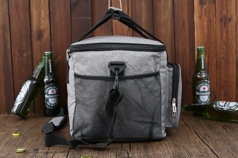 May include: A gray and black insulated cooler bag with a zippered front pocket and a mesh side pocket. The bag has a black adjustable shoulder strap and a top handle.
