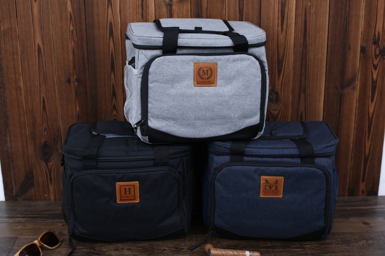 K&ouml;nnte beinhalten: Drei isolierte Lunch-Taschen mit personalisierten Leder-Patches. Die Taschen sind grau, schwarz und blau. Die Patches haben die Initialen "M", "H" und "M".