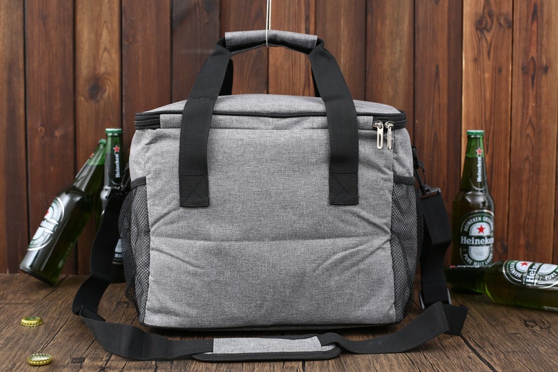 May include: A gray insulated cooler bag with black straps and a zipper closure. The bag has a mesh side pocket and a shoulder strap.