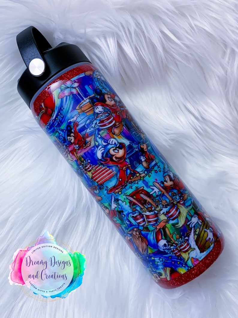 May include: A red glitter tumbler with a black lid and handle. The tumbler features a colorful illustration of Mickey Mouse and other Disney characters. The text "Dreamy Designs and Creations" is printed on a rainbow circle sticker on the tumbler.