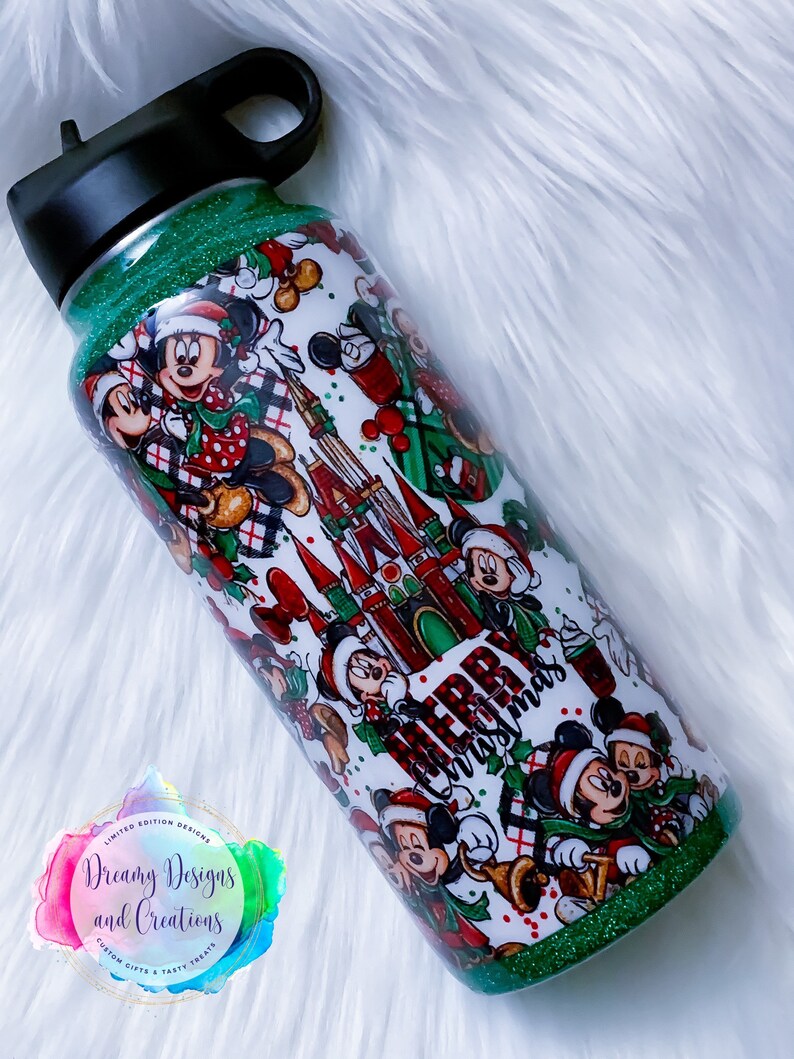Pode incluir: Garrafa de &aacute;gua de a&ccedil;o inoxid&aacute;vel com glitter verde sobre um fundo branco com um design de Natal com os personagens Mickey Mouse e Minnie Mouse, as palavras "Feliz Natal" e o Castelo da Cinderela.