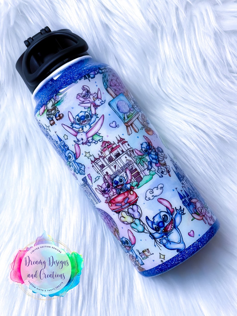 Op de afbeelding: Een blauwe en witte roestvrijstalen waterfles met een zwarte dop. De fles is versierd met een cartoonfiguur en verschillende kleurrijke ontwerpen. De fles heeft een glitterafwerking.