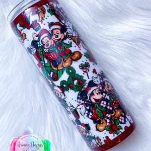Pode incluir: Um copo branco com uma borda de glitter vermelha e um design tem&aacute;tico de Natal com o Mickey Mouse e seus amigos. O design inclui o Mickey Mouse, a Minnie Mouse, o Pluto e o Pateta usando chap&eacute;us de Papai Noel e roupas tem&aacute;ticas de Natal. O copo &eacute; decorado com azevinho, bengalas de doces e outros elementos natalinos.