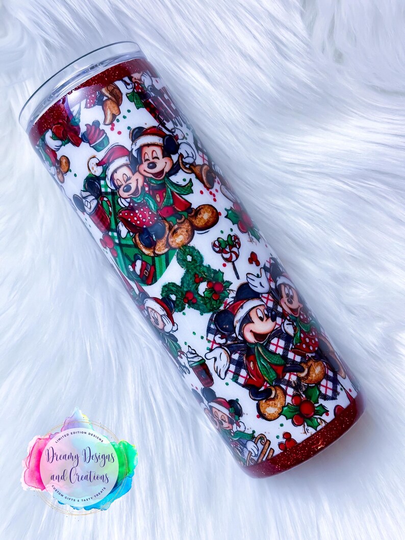 Pode incluir: Um copo branco com uma borda de glitter vermelha e um design tem&aacute;tico de Natal com o Mickey Mouse e seus amigos. O design inclui o Mickey Mouse, a Minnie Mouse, o Pluto e o Pateta usando chap&eacute;us de Papai Noel e roupas tem&aacute;ticas de Natal. O copo &eacute; decorado com azevinho, bengalas de doces e outros elementos natalinos.