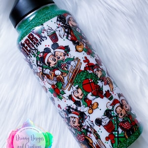 Pode incluir: Um copo verde com glitter com fundo branco que apresenta um padr&atilde;o repetido de personagens do Mickey Mouse e Minnie Mouse com trajes de Natal. O texto "Merry Christmas" &eacute; vis&iacute;vel no copo.