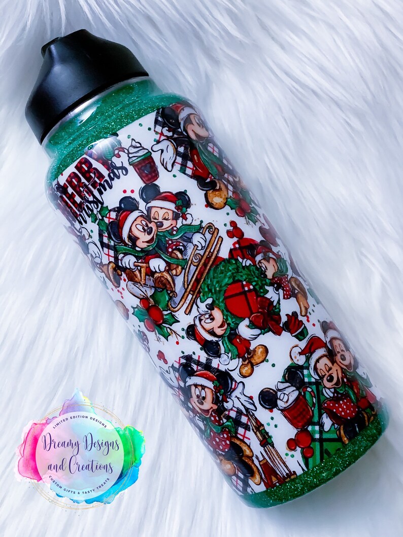 Pode incluir: Um copo verde com glitter com fundo branco que apresenta um padr&atilde;o repetido de personagens do Mickey Mouse e Minnie Mouse com trajes de Natal. O texto "Merry Christmas" &eacute; vis&iacute;vel no copo.