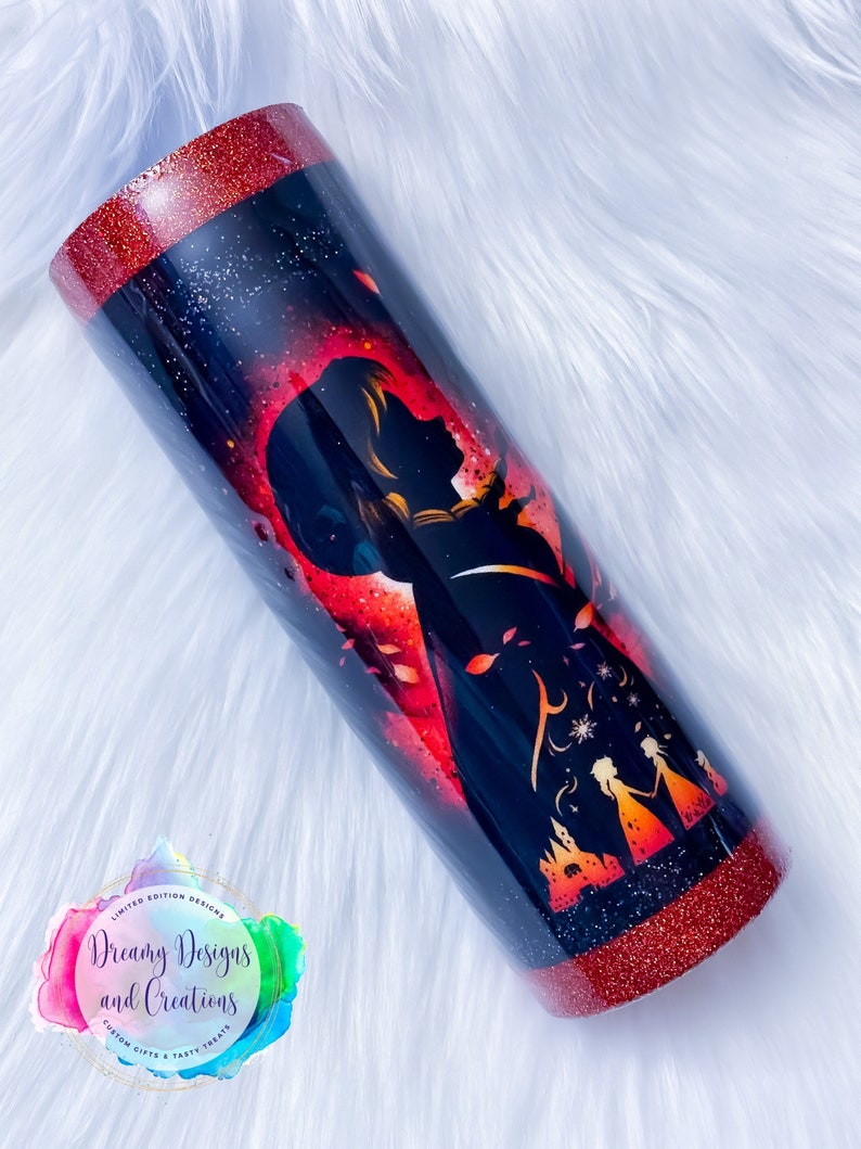 Op de afbeelding: Een rode en zwarte glitterbeker met een silhouet van een vrouw en een kasteel. De beker heeft een rode glitterrand en -basis. De tekst "Dreamy Designs and Creations" staat op de beker.