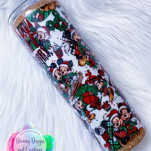 Pode incluir: Um copo branco com uma borda e base de glitter dourado. O copo &eacute; coberto com um padr&atilde;o de Natal com Mickey Mouse e Minnie Mouse em v&aacute;rias poses. O padr&atilde;o inclui xadrez vermelho e verde, azevinho e enfeites. O texto "Feliz Natal" &eacute; vis&iacute;vel no copo.