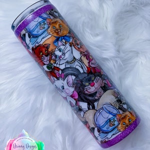 May include: A purple glitter tumbler with a white background featuring a colourful illustration of various cats from the Disney movie The Aristocats. The tumbler has a purple glitter rim and base.