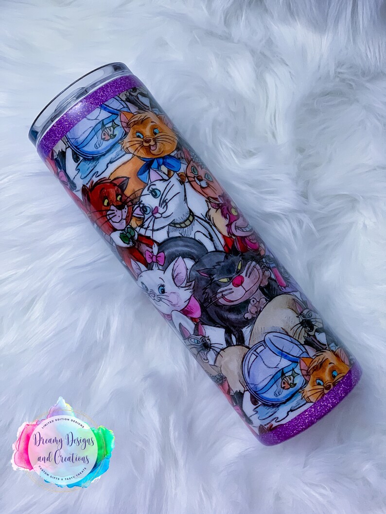 May include: A purple glitter tumbler with a white background featuring a colourful illustration of various cats from the Disney movie The Aristocats. The tumbler has a purple glitter rim and base.