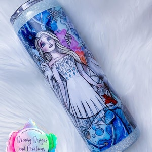 Puede incluir: Un vaso de acero inoxidable blanco y azul con purpurina, decorado con un dise&ntilde;o impreso de una mujer con el pelo largo y rubio que lleva un vestido blanco con un patr&oacute;n azul y blanco. El dise&ntilde;o tambi&eacute;n incluye copos de nieve, hielo y un caballo azul.