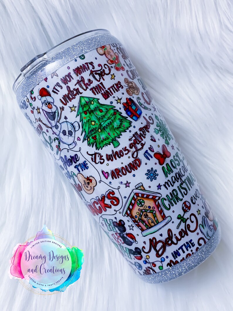 Pu&ograve; includere: Un bicchiere bianco con un bordo di glitter argentato e un design colorato con illustrazioni e testo a tema natalizio. Il testo include "Non &egrave; quello che c'&egrave; sotto l'albero che conta", "&Egrave; chi si riunisce intorno", "Il Natale pi&ugrave; magico di sempre", e "Credi nella magia".