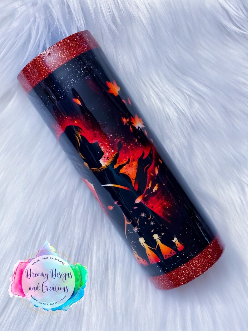 Op de afbeelding: Een zwarte en rode glitterbeker met een silhouet van een vrouw en twee kinderen voor een rode en oranje achtergrond. De beker heeft een rode glitterrand en -basis. De tekst "Dreamy Designs and Creations" staat op de beker.