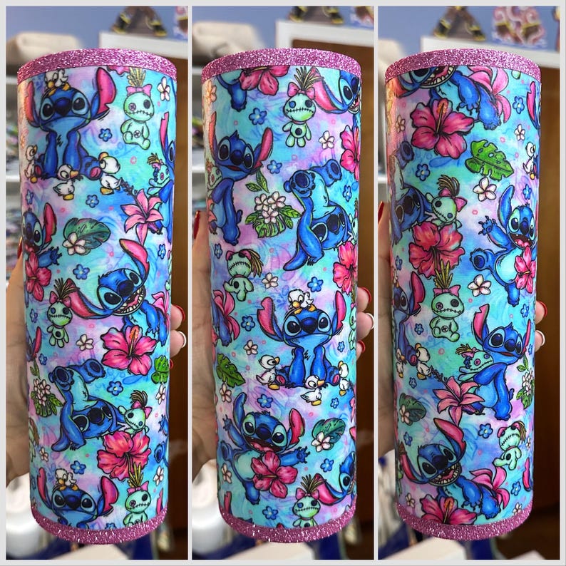May include: A stainless steel tumbler with a pink glitter rim and a blue and white pattern featuring Stitch from Lilo & Stitch. The pattern includes flowers, leaves, and other tropical elements.