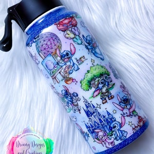 Op de afbeelding: Een blauwe en witte waterfles van roestvrij staal met een zwarte dop en handvat. De fles is versierd met een patroon van Stitch-personages uit Disney's Lilo & Stitch, samen met verschillende Disney-parkiconen, waaronder Assepoester's kasteel, Spaceship Earth en de Tree of Life. De fles heeft een blauwe glitterafwerking.