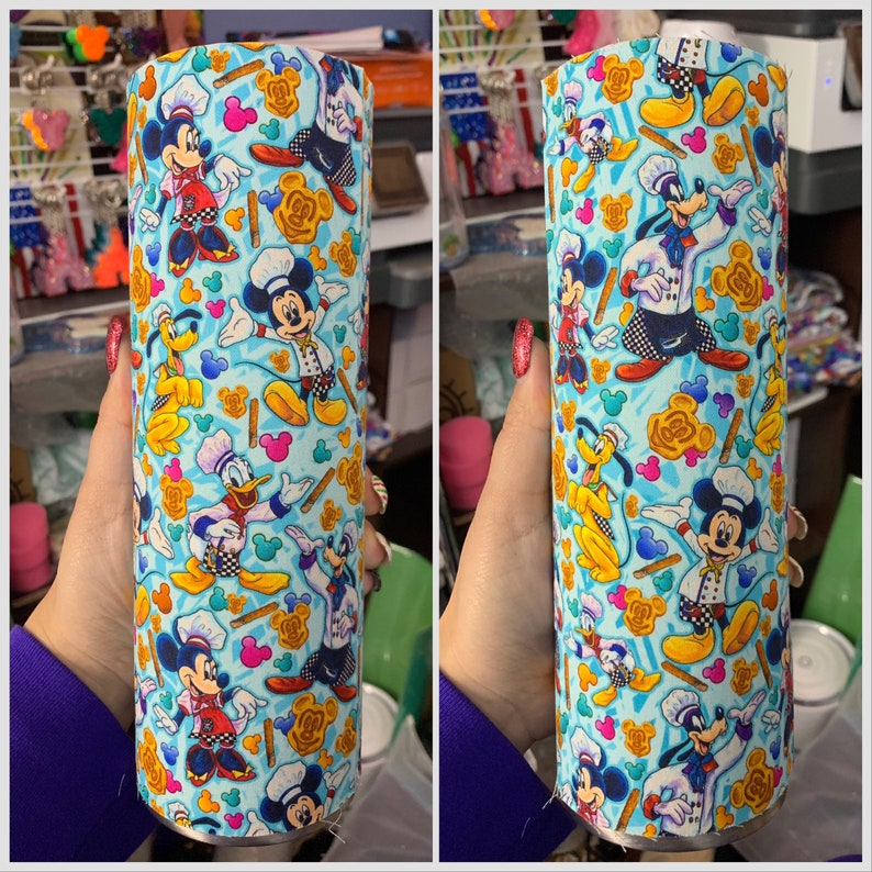 Puede incluir: Un vaso de acero inoxidable con fondo azul y un patr&oacute;n repetido de Mickey Mouse, Donald Duck y Goofy vestidos de chefs. El patr&oacute;n tambi&eacute;n incluye orejas de Mickey Mouse, gorros de chef y cucharas de madera.