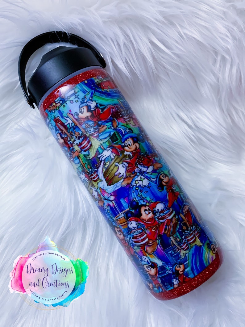 May include: A red and blue stainless steel tumbler with a handle. The tumbler is covered in a colorful print of Mickey Mouse and other Disney characters. The tumbler has a glitter finish and says "Dreamy Designs and Creations" on the bottom.