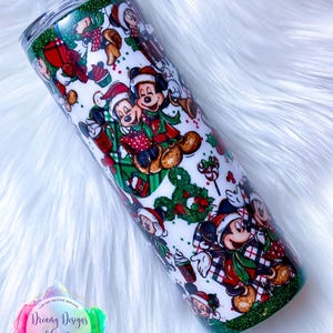 Pode incluir: Um copo branco com fundo de glitter verde. O copo apresenta um design tem&aacute;tico de Natal com Mickey Mouse e seus amigos usando chap&eacute;us de Papai Noel e segurando presentes. O design &eacute; repetido em todo o copo.