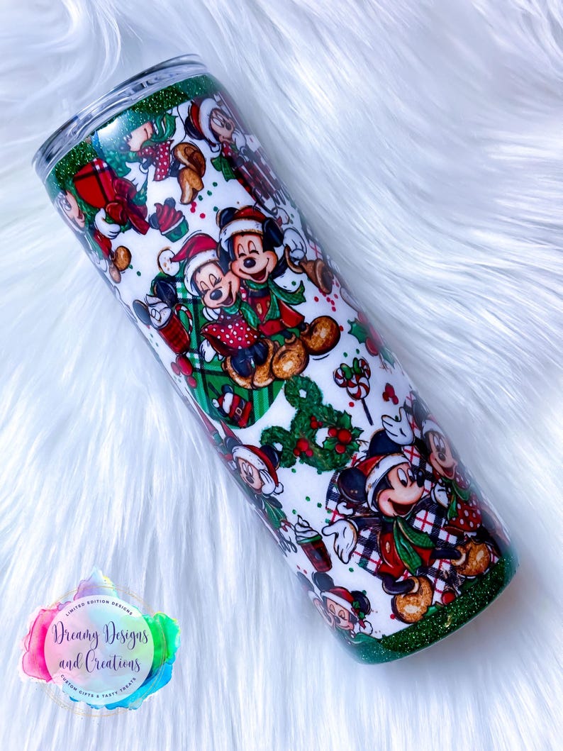 Pode incluir: Um copo branco com fundo de glitter verde. O copo apresenta um design tem&aacute;tico de Natal com Mickey Mouse e seus amigos usando chap&eacute;us de Papai Noel e segurando presentes. O design &eacute; repetido em todo o copo.
