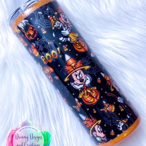 May include: A black and orange stainless steel tumbler with a Halloween-themed design featuring Mickey Mouse and Minnie Mouse dressed in witch costumes. The tumbler has a glitter finish and features candy corn, pumpkins, and spiderwebs. The text "BOO!" is printed on the tumbler.