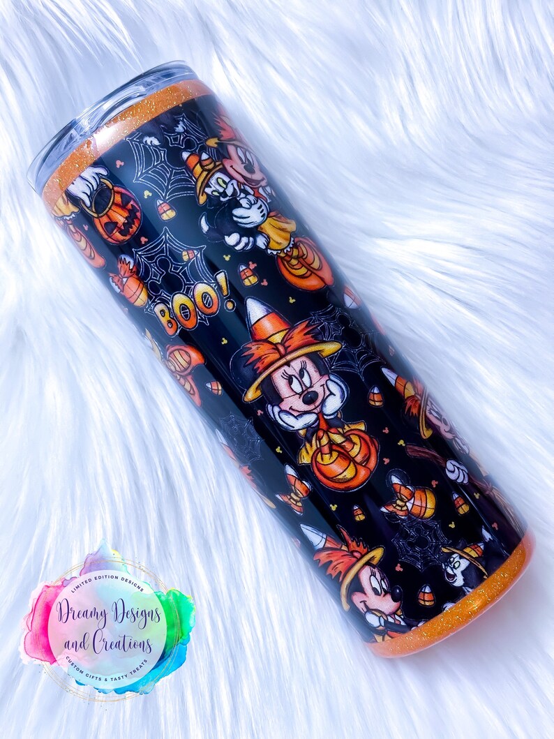 May include: A black and orange stainless steel tumbler with a Halloween-themed design featuring Mickey Mouse and Minnie Mouse dressed in witch costumes. The tumbler has a glitter finish and features candy corn, pumpkins, and spiderwebs. The text "BOO!" is printed on the tumbler.