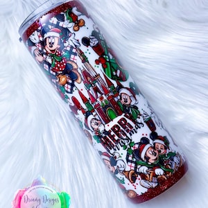 Pode incluir: Um copo vermelho e branco com tema natalino com Mickey Mouse e as palavras "Feliz Natal". O copo &eacute; coberto com um padr&atilde;o de personagens do Mickey Mouse, &aacute;rvores de Natal e o Castelo da Cinderela.