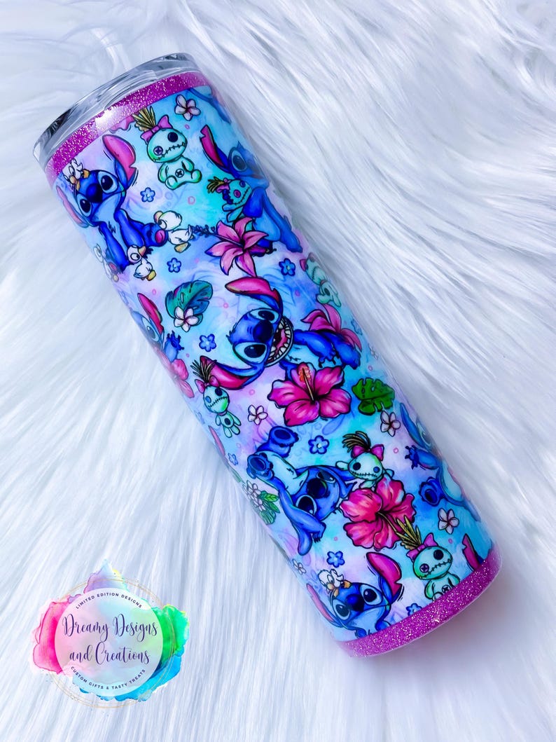 May include: A stainless steel tumbler with a pink glitter rim and a blue and white design featuring Stitch characters from the Disney movie Lilo & Stitch. The tumbler is decorated with flowers and a watercolor background.