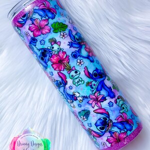 May include: A blue and pink stainless steel tumbler with a glitter rim. The tumbler features a repeating pattern of Stitch from Lilo & Stitch, tropical flowers, and leaves. The text "Dreamy Designs and Creations" is visible on the tumbler.