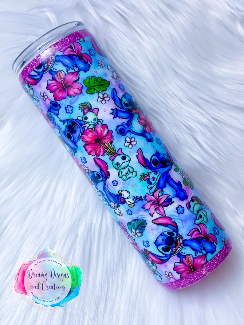 May include: A blue and pink stainless steel tumbler with a glitter rim. The tumbler features a repeating pattern of Stitch from Lilo & Stitch, tropical flowers, and leaves. The text "Dreamy Designs and Creations" is visible on the tumbler.